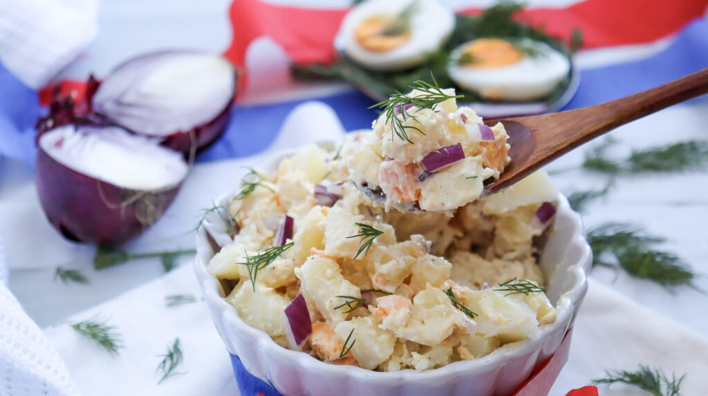 Potato salad being served with a large, wooden spoon.