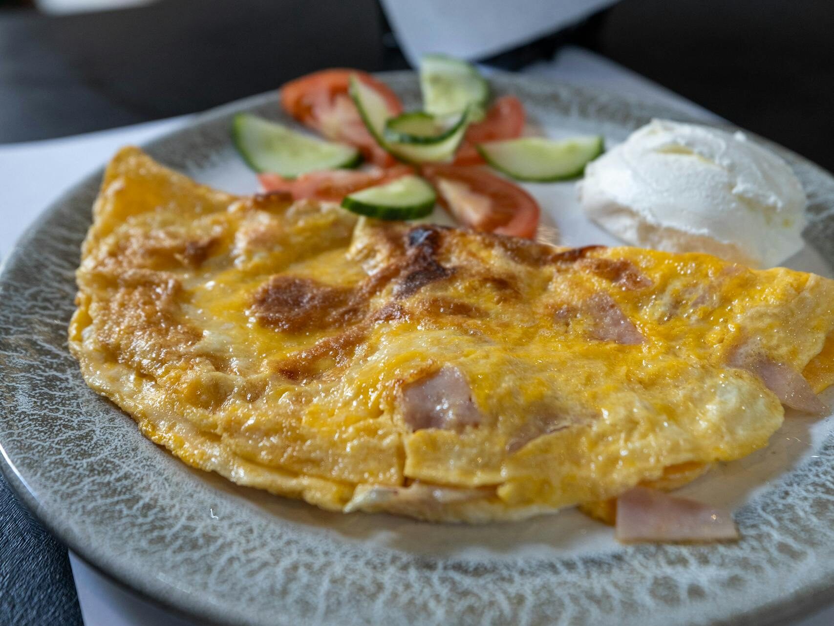 Close-up of a ham and cheese omelet with cucumber, tomato and a bread roll.