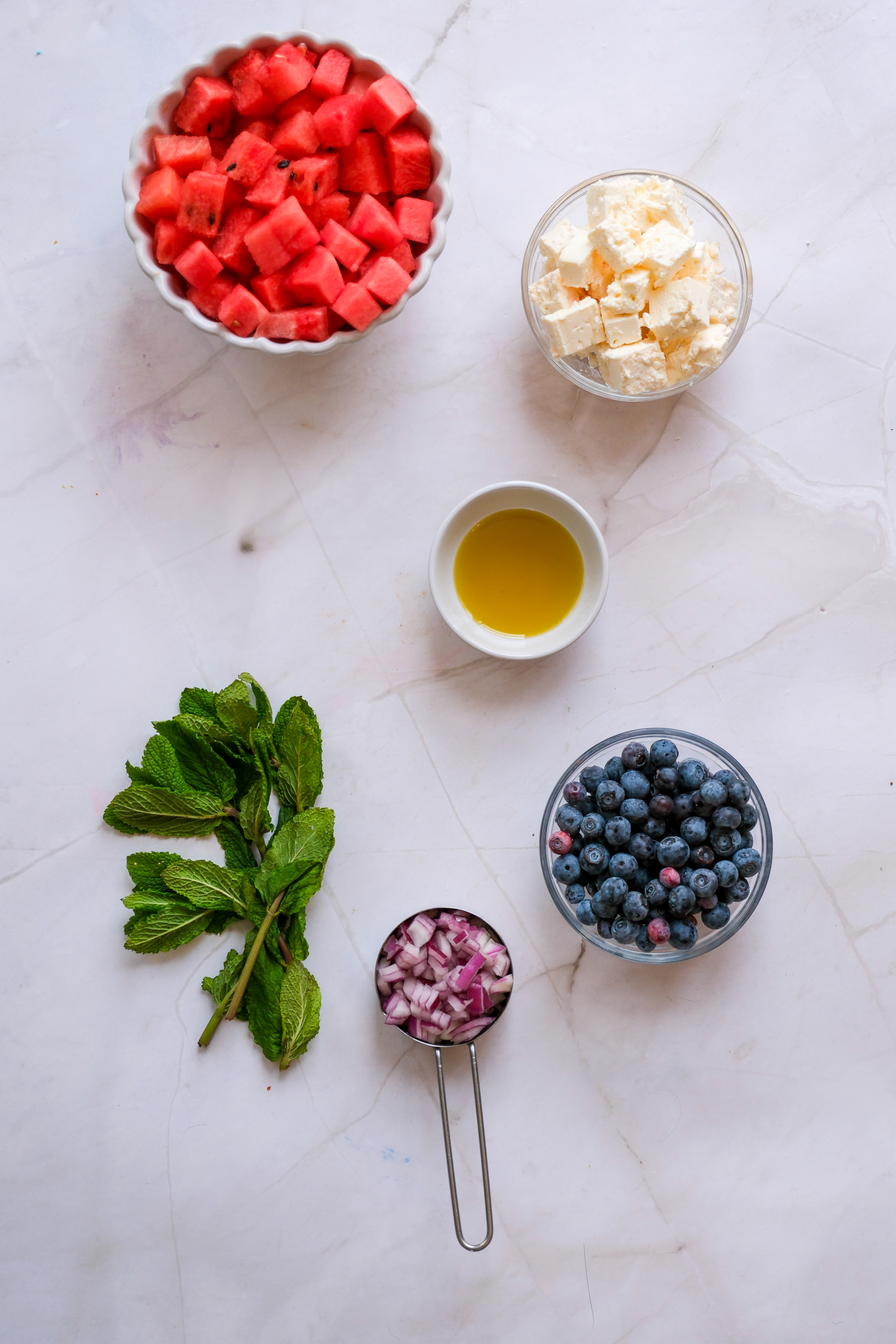 Ingredients of the Watermelon and Feta Salad laid out separately on a white marble countertop.