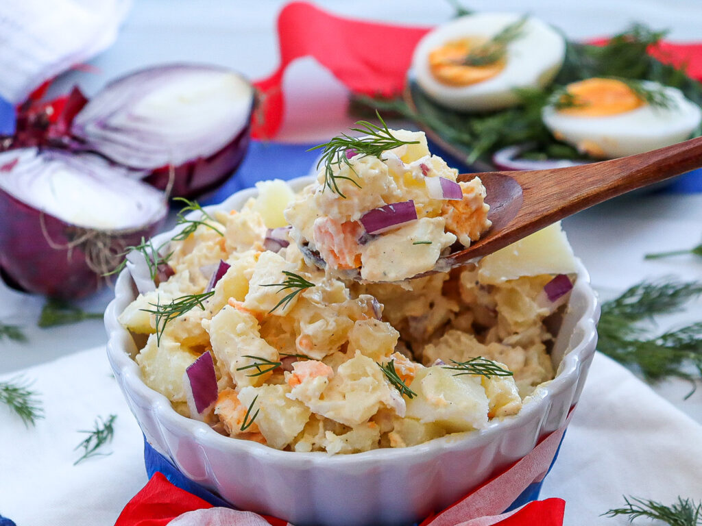 Easy side dishes for barbecues - classic Potato Salad being served out of a white dish with a wooden spoon.