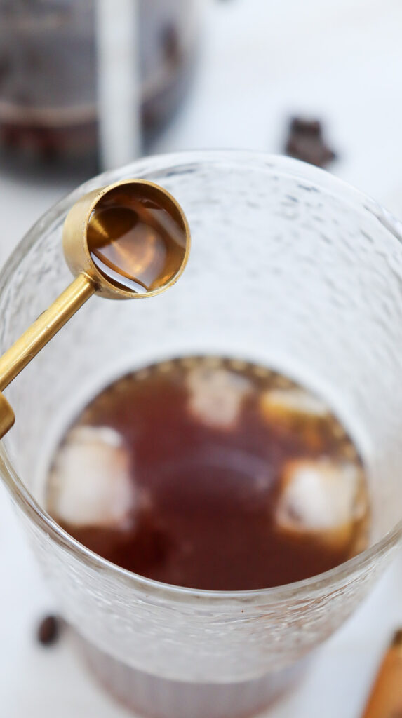 Pouring vanilla extract into caramel iced coffee.
