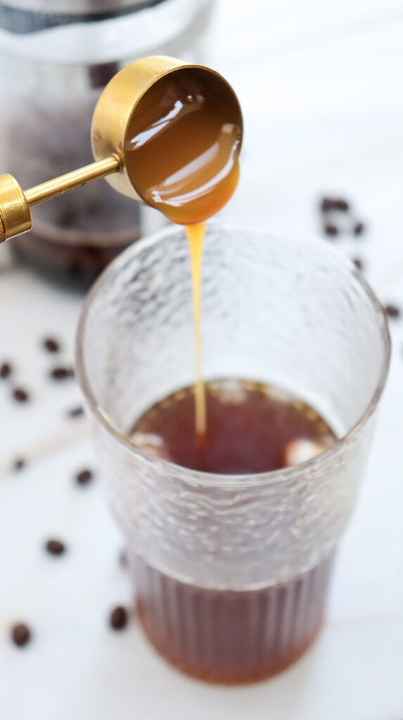 Pouring caramel sauce into caramel iced coffee.
